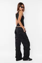 Pantalón cargo color arena de corte recto y tiro bajo, con recortes y presillas dobles en la cintura. Tiene acceso mediante cierre de nylon y botón personalizado, seis bolsillos laterales y dos en la espalda con tapa y botón snap a presión.