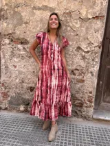 Vestido largo de seda con estampado tie-dye en tonos rojo y blanco, con mangas cortas con volados y ruedo con volados.