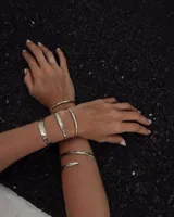 Pulsera tipo esclava abierta, con acabado rústico y textura irregular, en tono plateado. Se vende por unidad.