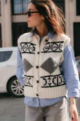 Chaleco de lana tejido a mano con diseño jacquard en negro, blanco y gris. Tiene cuello redondo y cierre frontal con botones de cuero.