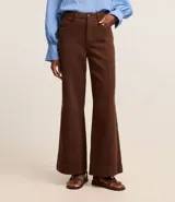 Pantalón wide leg de sarga color marrón chocolate, con cintura alta, trabillas, bolsillos delanteros y traseros, cierre con botón y cremallera, y costura vertical delantera.