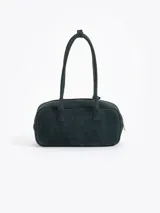 Cartera rectangular de estructura firme confeccionada en cuero descarne vacuno color marrón. Presenta manijas fijas, cierre superior y un charm metálico dorado en forma de vaquita de San Antonio colgando de un tag lateral. Incluye el logo de la marca grabado en relieve en el frente.