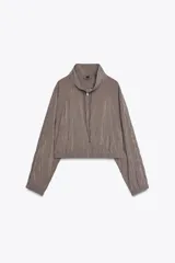 Chaqueta corta color gris topo, confeccionada en hilatura con mezcla de modal, con cuello alto, cierre frontal con cremallera metálica, bolsillos laterales y mangas largas con puños elásticos.