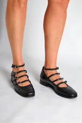 Chatas de cuero negro con punta fina, cuatro tiras horizontales con hebilla y pulsera al tobillo.