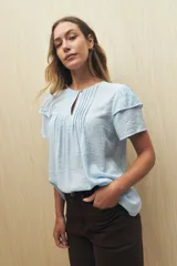 Blusa blanca de tela liviana con mangas cortas con volados y botón de nácar.