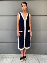 Vestido tipo chaleco azul marino con ribetes blancos, cuello en V, botones dorados y bolsillos frontales.