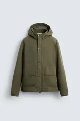 Parka verde militar de tejido técnico ligero resistente al viento, con cuello alto, capucha y manga larga con puños ajustables. Tiene bolsillos de plastrón con solapa en la cadera, bolsillo interior y bajo ajustable con elásticos. El cierre frontal es con cremallera oculta por solapa con botones a presión.