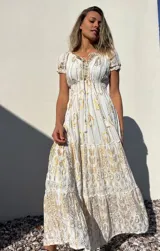 Vestido largo blanco con estampado dorado, escote en V con cordones y mangas cortas abullonadas.