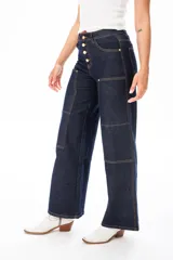 Pantalón de jean azul oscuro, de corte ancho, con bolsillos frontales y traseros. Presenta cierre frontal con botones dorados.