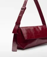 Bolso de hombro tipo baguette color blanco hueso, con textura craquelada y acabado brillante. Cierre magnético con solapa frontal y asa corta regulable.