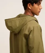 Campera rompevientos color verde oliva, con capucha ajustable con cordón, cierre frontal con cremallera, bolsillos laterales con cremallera y puños elásticos.