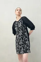 Vestido corto blanco de algodón con bordado floral en relieve, escote redondo con abotonadura frontal y mangas amplias.