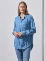Camisa de jean celeste con flecos en el ruedo, de mangas largas y corte recto.