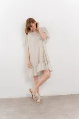 Vestido corto color beige confeccionado en algodón, con escote en V con detalles bordados, mangas cortas amplias con volados y falda con ruedo en volado.