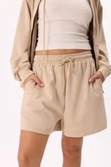 Conjunto deportivo color marrón, compuesto por un buzo con capucha, cierre frontal, bolsillos y terminaciones metálicas, y un short con cintura elástica ajustable con cordón.