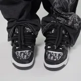 Zapatillas de skate negras con estampado de logos en blanco y gris, cordones gruesos negros, suela blanca y detalles en ecocuero.