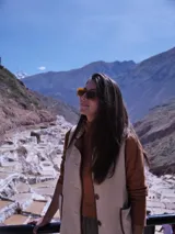 Chaleco color crema con cuello y borde de cuero marrón, con cierre de botones y bolsillos frontales.