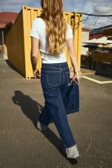 Jean de tiro superalto con pierna amplia y corte holgado. Presenta un diseño de cinco bolsillos, cierre con botón y un doblez ancho en el bajo que deja ver el revés de la tela. Confeccionado en denim con estampado de rayas finas verticales.