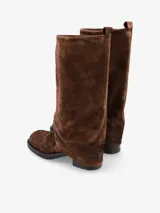 Bota de caña alta confeccionada en cuero negro con sutiles matices marrones de efecto desgastado. Presenta un diseño de caña doble o solapada que cubre parte del empeine, silueta recta, punta redondeada y taco bajo cuadrado.