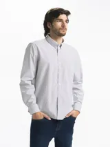 Camisa celeste y blanca a rayas verticales, de manga larga y corte clásico. Tiene cuello abotonado y bolsillo en el pecho.