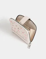 Billetera pequeña de cuerina color crema con estampado de flores pequeñas, cierre perimetral con cremallera y broche con botón a presión.