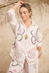Conjunto de camisa de manga larga con cuello y pantalón palazzo, ambos con estampado de flores y hojas en tonos rosa, gris y marrón sobre fondo blanco.