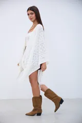 Poncho blanco de tejido calado con diseño geométrico y flecos en el borde.