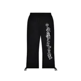 Conjunto deportivo negro de buzo con capucha y pantalón de jogging, ambos con logo "Trapstar" en letras góticas blancas con contorno plateado. El buzo tiene cierre frontal y bolsillo tipo canguro. El pantalón tiene cordón ajustable en la cintura y tobillos ajustables.