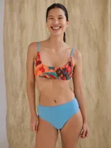 Top de bikini deportivo con estampado abstracto en tonos naranja, marrón y beige. Tiene tirantes finos con diseño a rayas verticales de colores.
