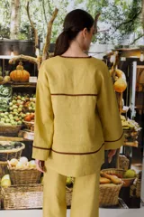 Blusa color crudo de lino con cuello en V y ribete marrón.