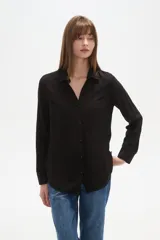 Camisa de manga larga, color negro, con cuello camisa y dos bolsillos frontales. Presenta un corte al cuerpo y está confeccionada en viscosa.
