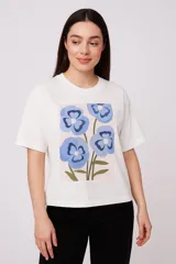 Remera blanca de corte recto con estampado de flores abstractas en tonos azules, verdes y rosados.