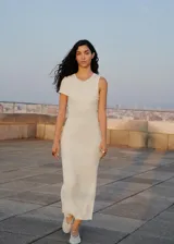 Vestido largo de punto acanalado color blanco roto, con cuello redondo y diseño entallado. Presenta un detalle asimétrico en el hombro derecho.