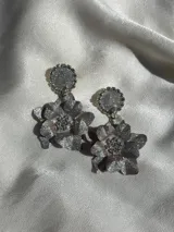 Par de aros colgantes plateados con forma de flor y detalles brillantes.