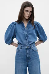 Blusa de denim con cuello solapa y manga abullonada por debajo del codo. Cierre frontal con botones.