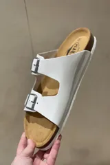 Sandalias blancas de cuero con doble tira y hebillas metálicas ajustables. Suela anatómica de corcho y goma.
