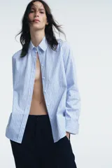Camisa de cuello solapa y manga larga con puño doble abotonado. Cierre frontal con botones y estampado a rayas verticales rosas y blancas.