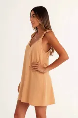 Vestido corto color amarillo mostaza, con escote en V y tirantes finos con detalle de volado o fruncido. El ruedo es asimétrico.