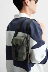 Bandolera vertical negra de acabado engomado con compartimento principal con cierre de cremallera y bolsillo interior plano. Bolsillo frontal con cierre de hebilla de liberación rápida. Asa de hombro ajustable y extraíble.