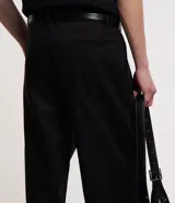 Pantalón negro de corte baggy confeccionado en sarga de sastrería, con cintura con trabillas, bolsillos y detalle de pliegues.