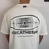 Remera blanca de corte clásico con estampado en la espalda que incluye un óvalo con diseño abstracto y la frase "BREATHEfast Feel the Vcp Concept Drift".