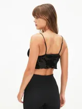 Top corto negro de tirantes finos, con escote en V y borde festoneado. El tejido es transparente con un estampado de terciopelo floral en relieve.