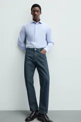 Camisa celeste a rayas verticales blancas, de corte recto, con cuello italiano abierto, mangas largas con puños abotonados y cierre frontal con botones.