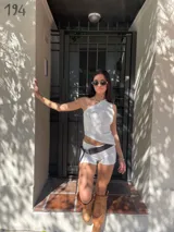 Conjunto de short y top blanco de un hombro. El top es ajustado y el short es de tiro alto con cinturón marrón.