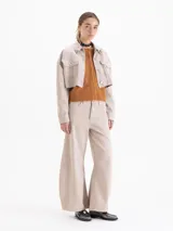 Chaqueta corta estilo jeanero, color beige claro, confeccionada en algodón. Presenta botones metálicos y remaches decorativos en el cuello.