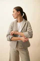 Chaqueta color crema de corte recto con cuello, solapa y bolsillos ojal. Forro solo en las mangas y terminaciones envivadas. Esquinas redondeadas y mangas con corte en puño que permiten transformarla en manga 3/4. Más larga en la espalda que en la delantera. Abrochadura con dos botones.