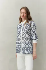 Camisa blanca de manga larga con bordado floral marrón, cuello clásico y cierre frontal con botones.