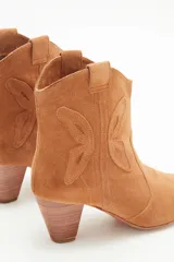 Bota corta de gamuza color camel, estilo cowboy, con taco medio de madera y recortes grabados en forma de mariposa en los laterales.