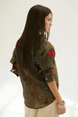 Camisa beige de manga larga con cuello clásico y cierre frontal con botones. Presenta bordados con motivos florales y geométricos en tonos azules, rojos y verdes.