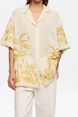 Camisa color crema con bordado de hojas color mostaza, de corte recto, manga corta y cuello camisero.
